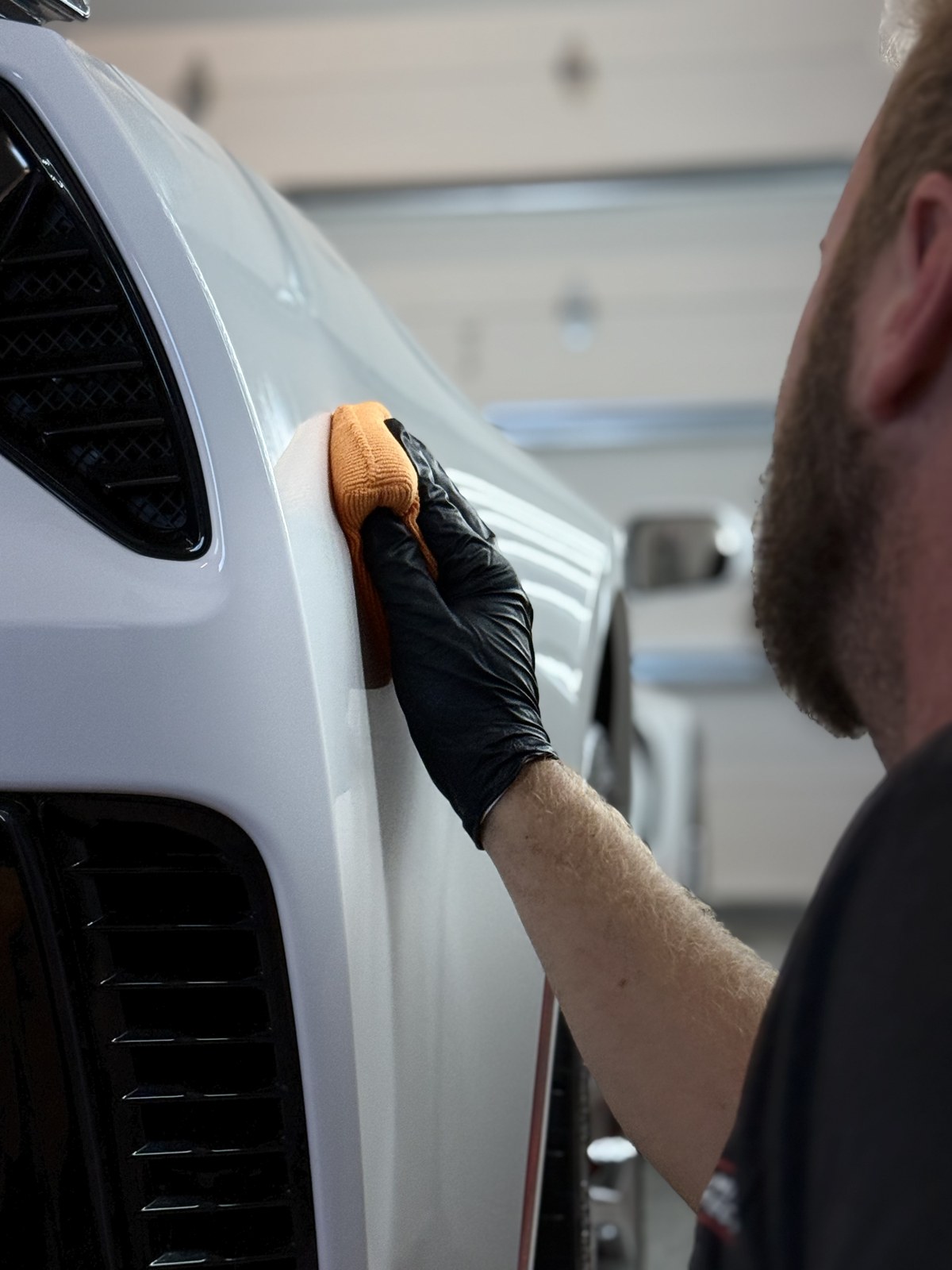 Detailed Motor Works installer hand-finishing STEK DYNOshield paint protection film on a white sports car front fender
